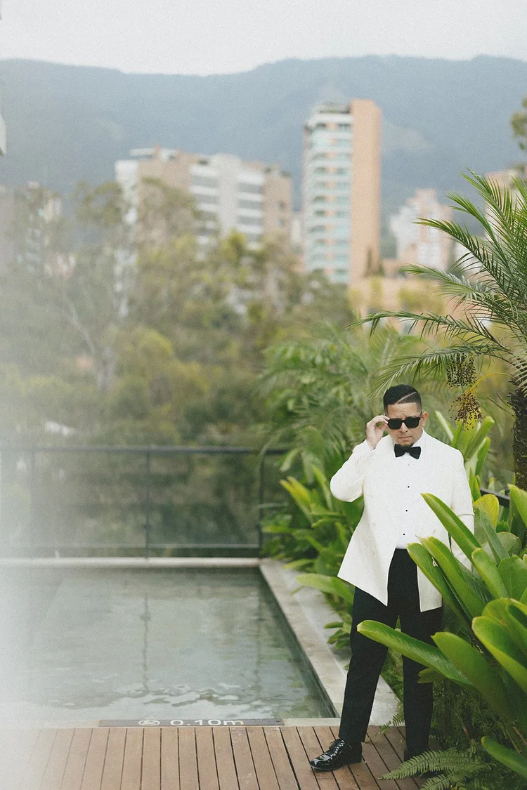 Film photo of Douglas in sunglasses and a cream jacket beside the pool with the Medellín skyline behind him