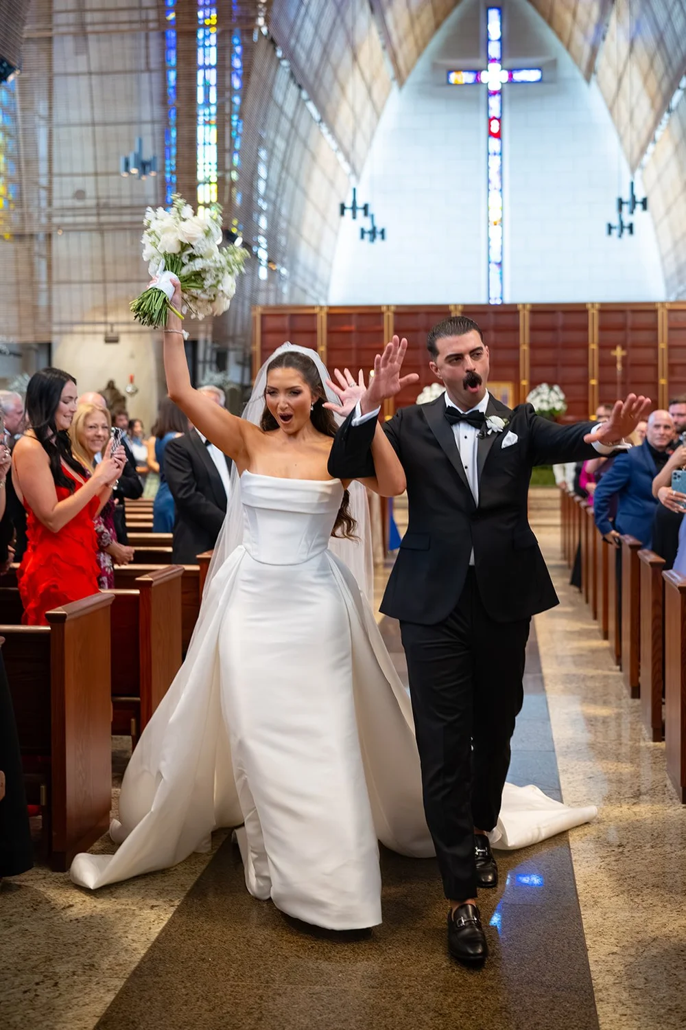 Rachel with her bouquet raised and Austin beside her as they walk back up the aisle after the ceremony