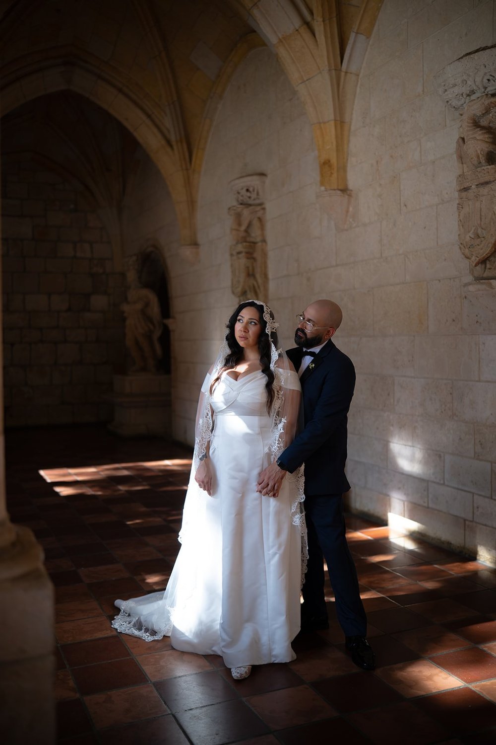 Maria and Christian standing together in a shaft of light in the monastery cloister