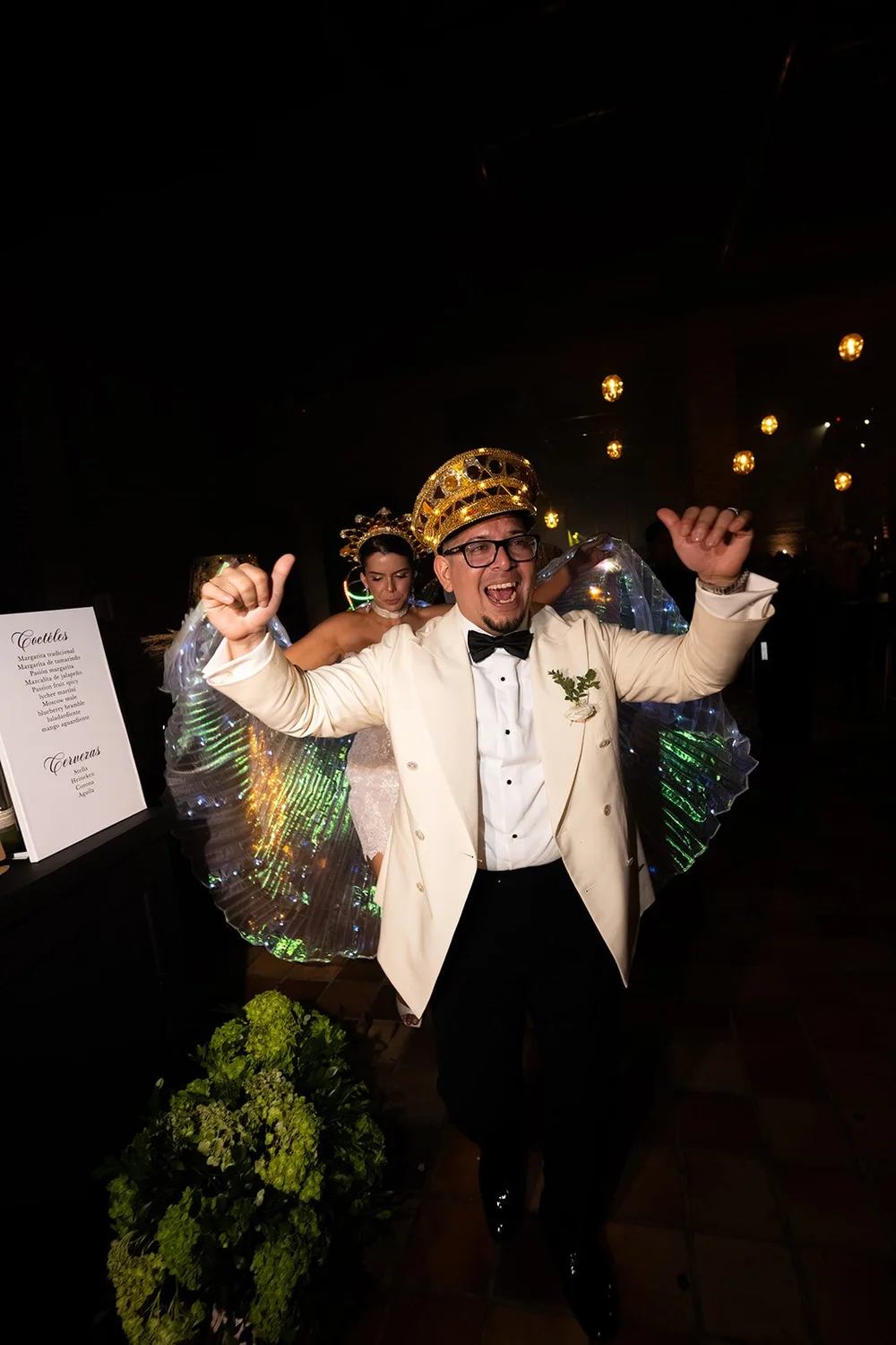 Douglas in a cream jacket and a gold crown dancing with guests in colorful costumes