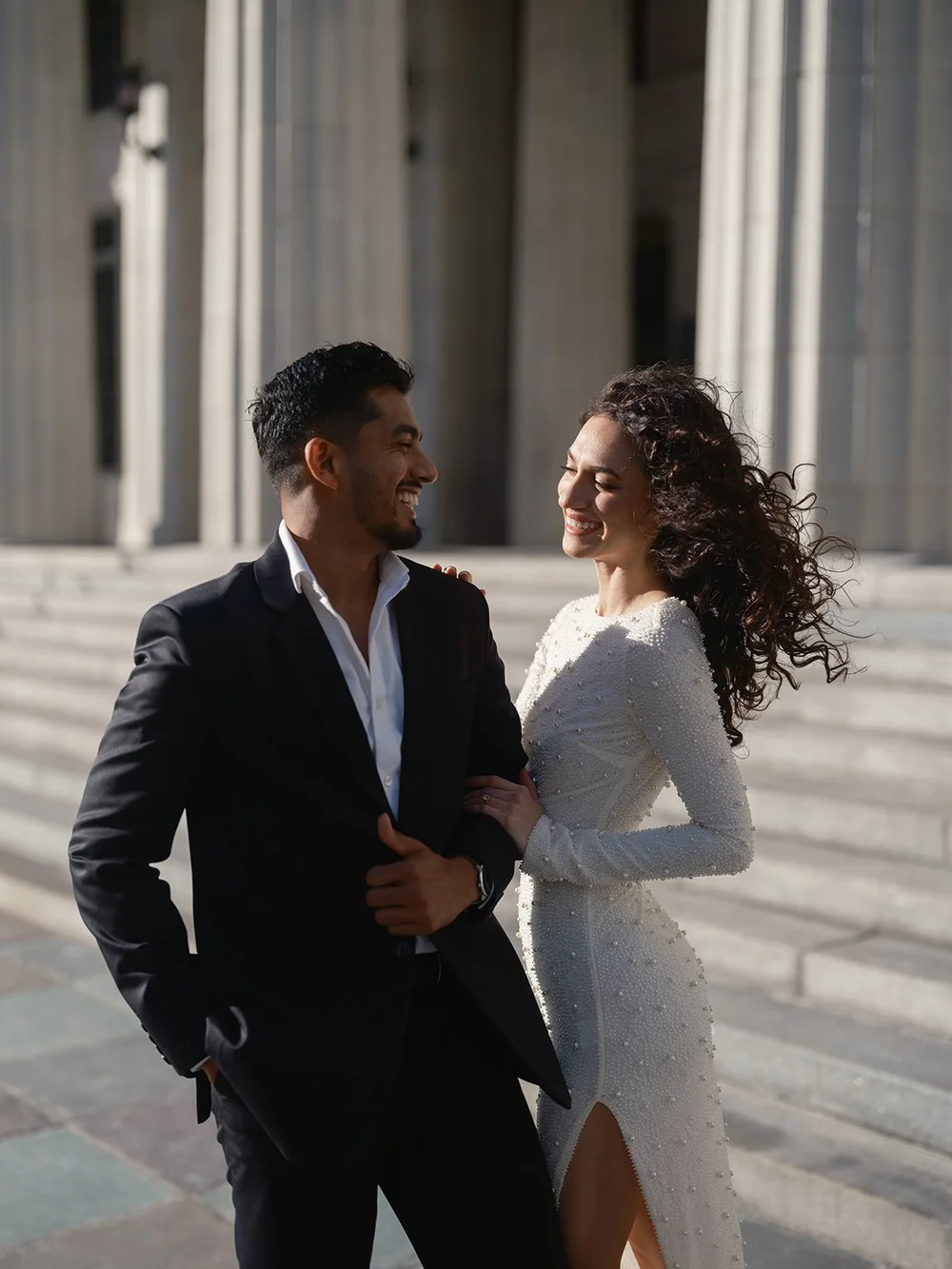 Groom smiling at the bride in a close portrait in front of the courthouse columns