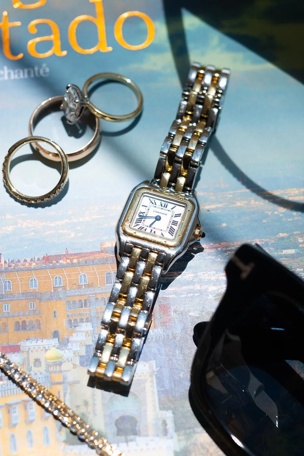 Wedding rings, a gold watch and a Portugal Encantado book laid out on a table