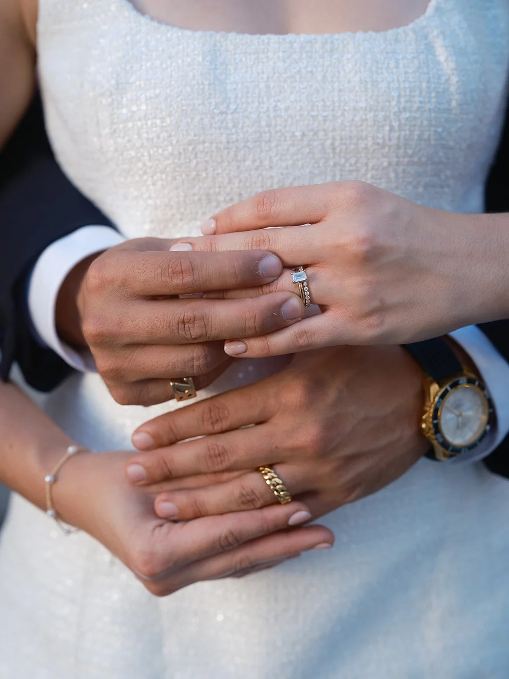 Detail of the couple's hands together showing their wedding rings against the white dress