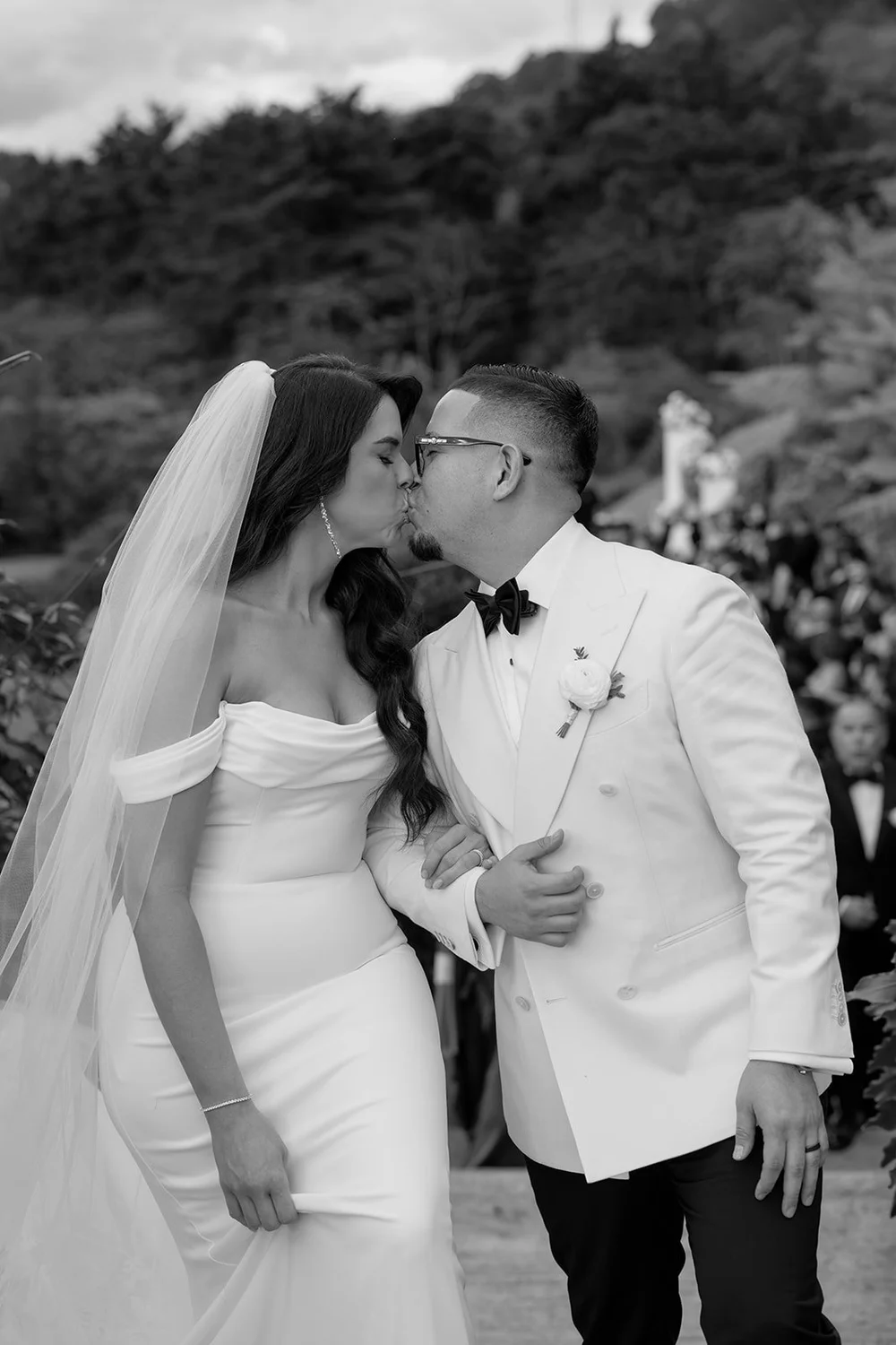 Black and white photo of Krystine and Douglas kissing with her veil blowing behind them