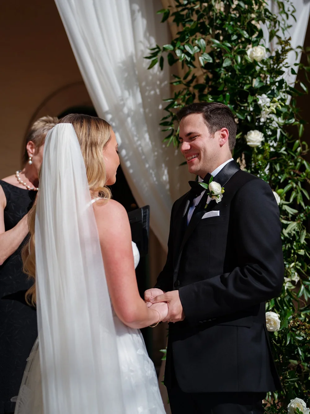 Jane and Berkeley holding hands during their vows in front of greenery and white drapes