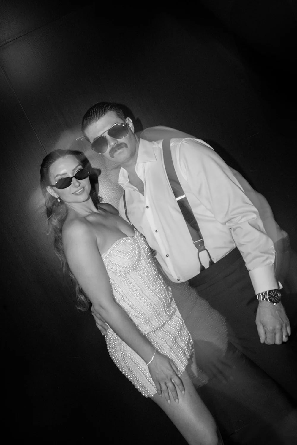 Rachel and Austin posing in sunglasses with flash during the party, in black and white