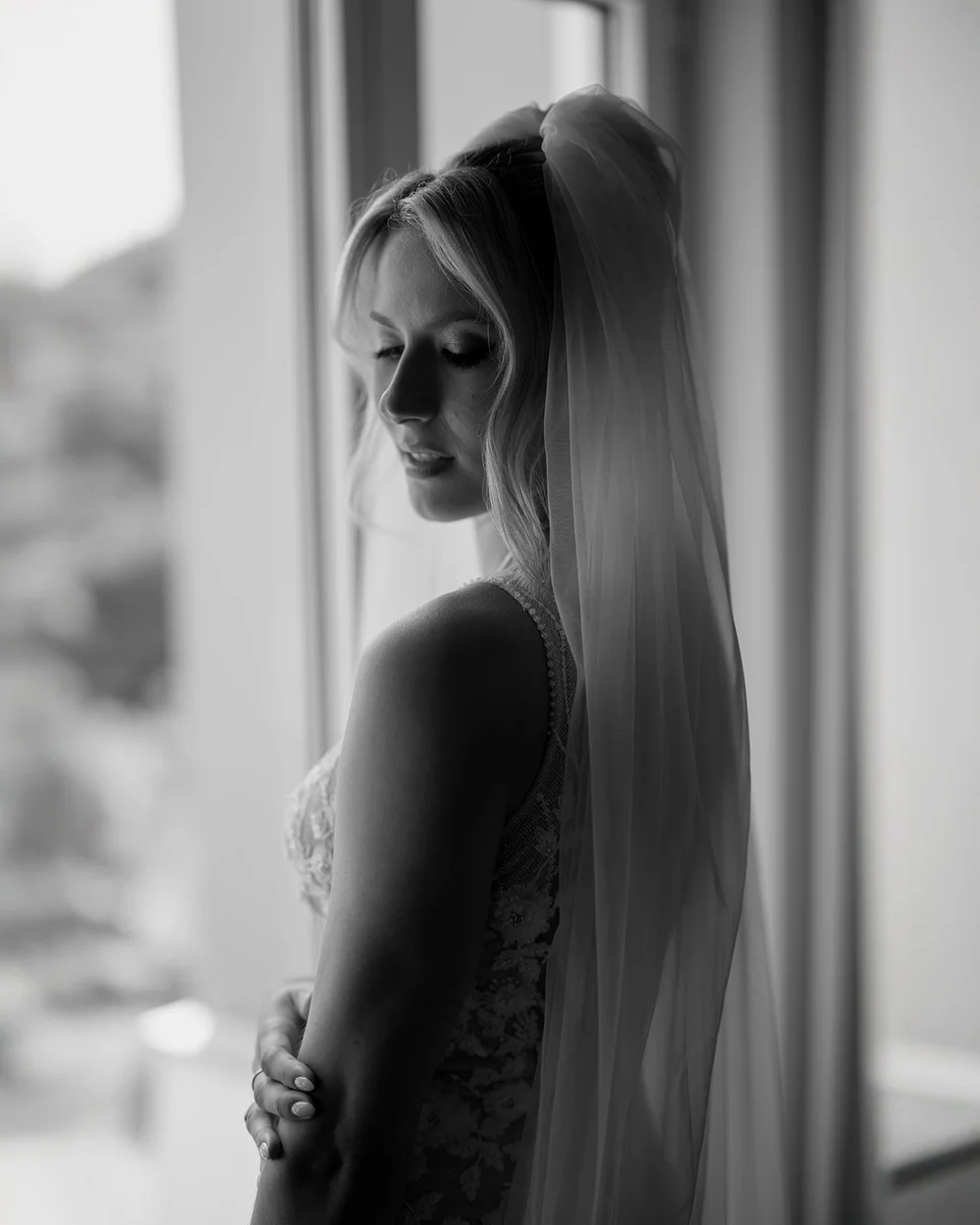 Black and white side profile of Ellen at a window in her long veil, eyes lowered and one hand resting on her arm
