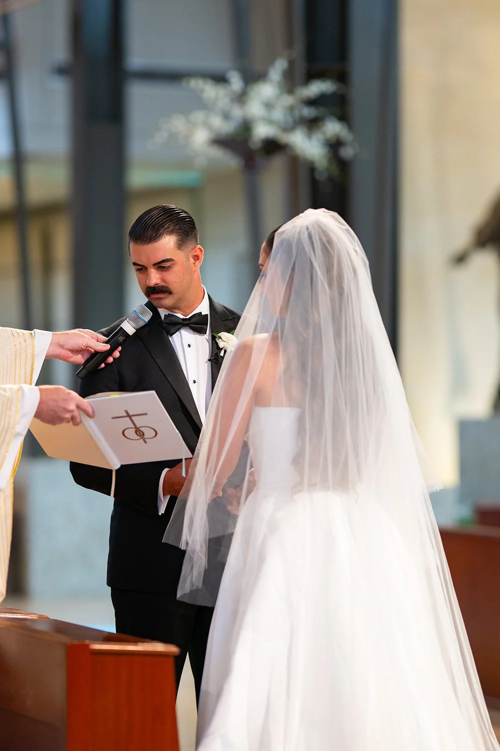 Austin reading his vows from a card while Rachel faces him at the altar in her veil