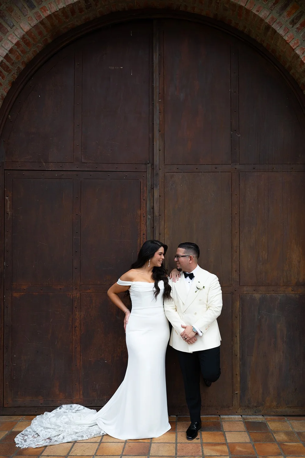 Krystine and Douglas standing in front of a large rust-brown wooden door