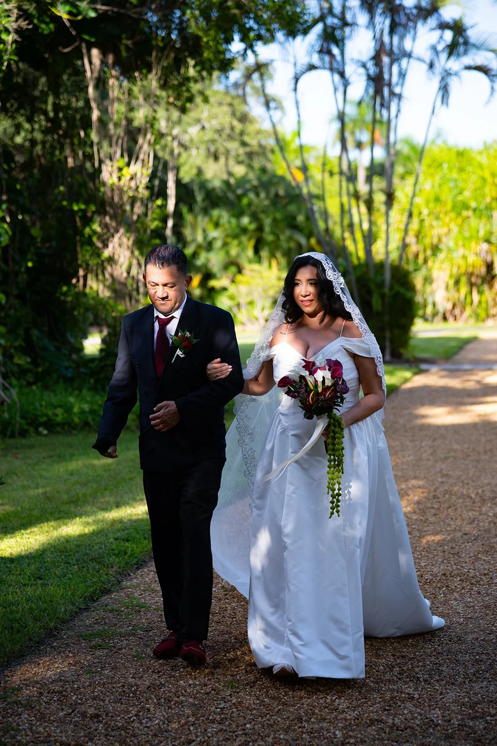 Maria carrying red and white roses as she walks down the garden path on the arm of her escort