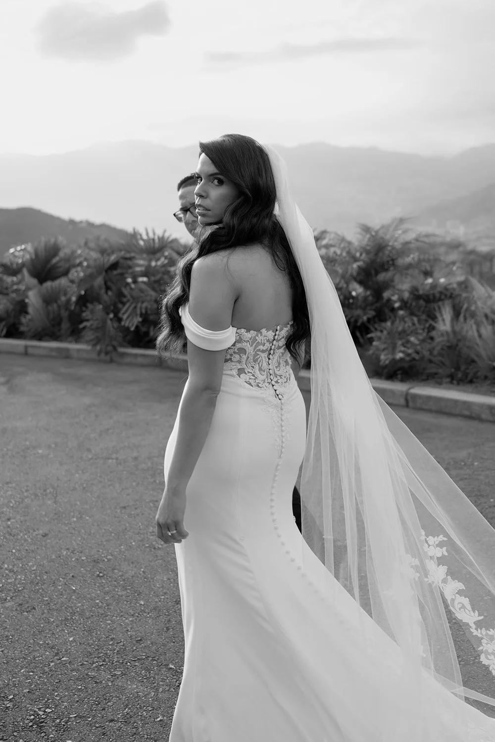 Black and white photo of Krystine looking back over her shoulder with her veil and the mountains behind her