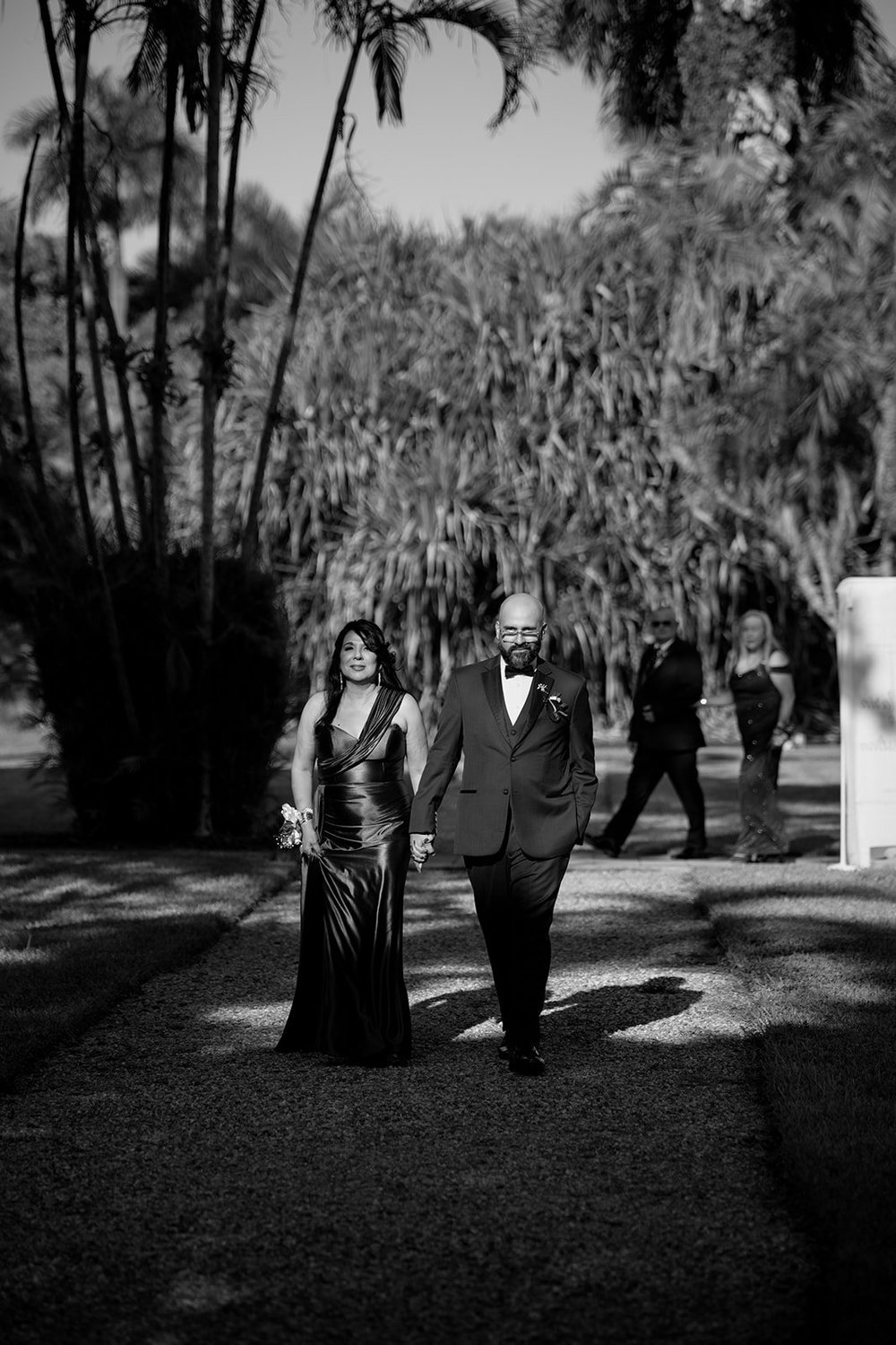 Guests in formal dress walking up the garden path to the ceremony, in black and white