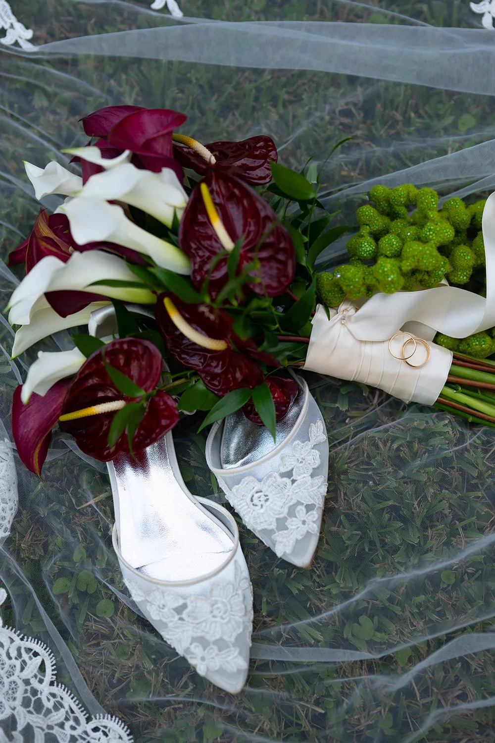 Red and white bouquet resting on lace beside Maria's white shoes