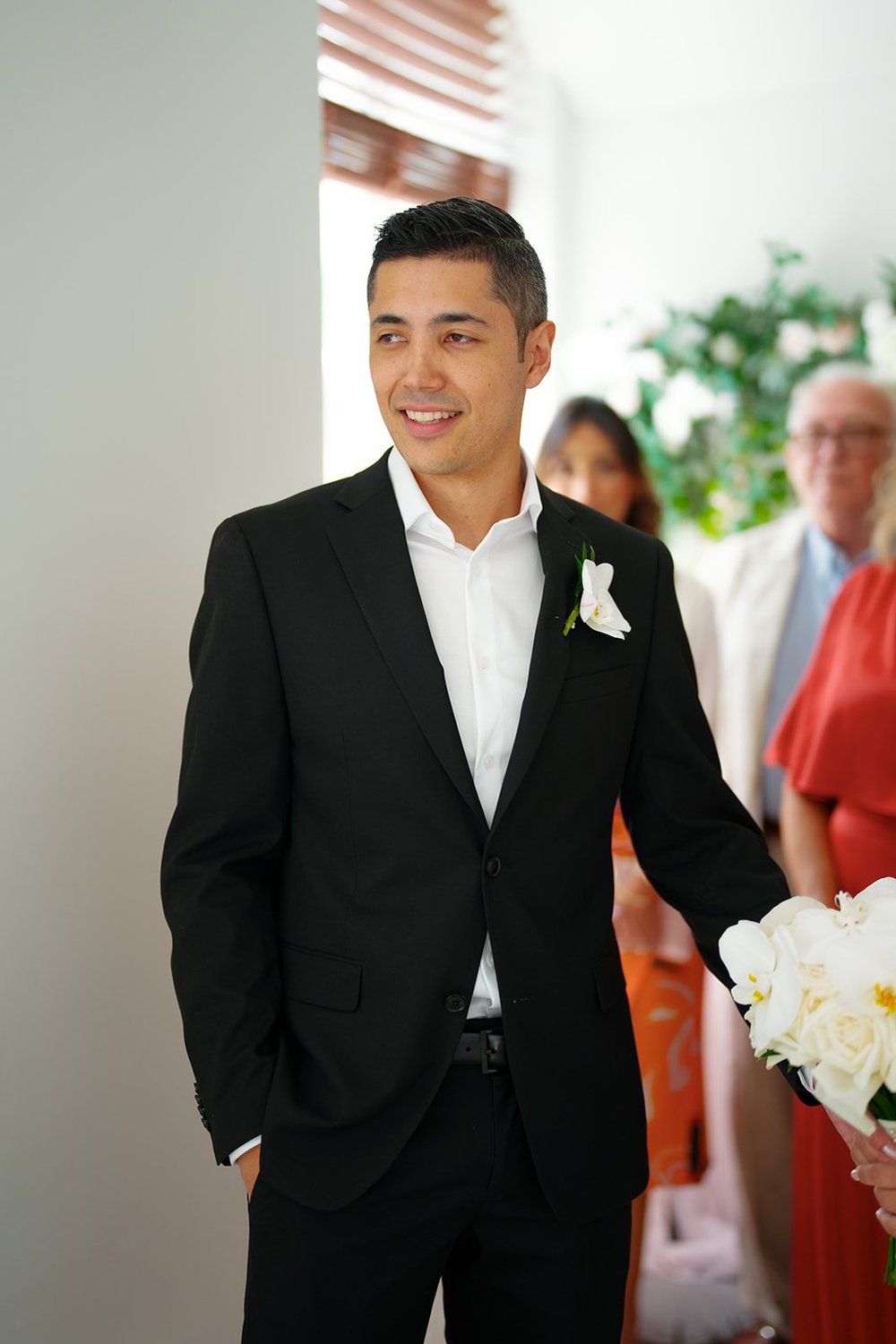 David in a black suit with a white boutonniere standing in front of guests
