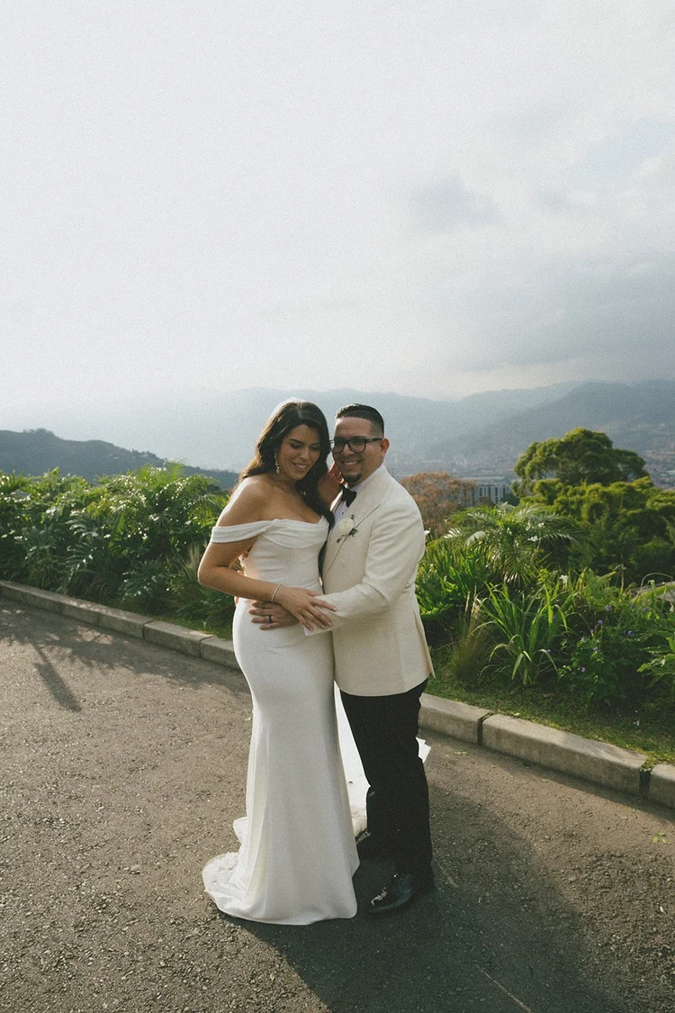 Film photo of Krystine and Douglas smiling together on a road with green hills and mountains behind them
