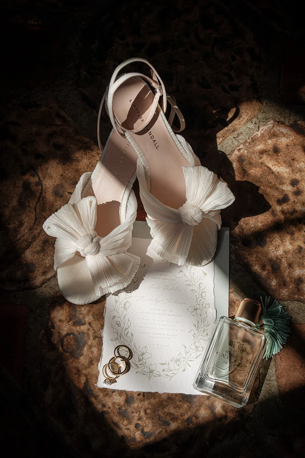 Jane's white bow heels on the Powel Crosley Estate wedding invitation with gold rings and perfume
