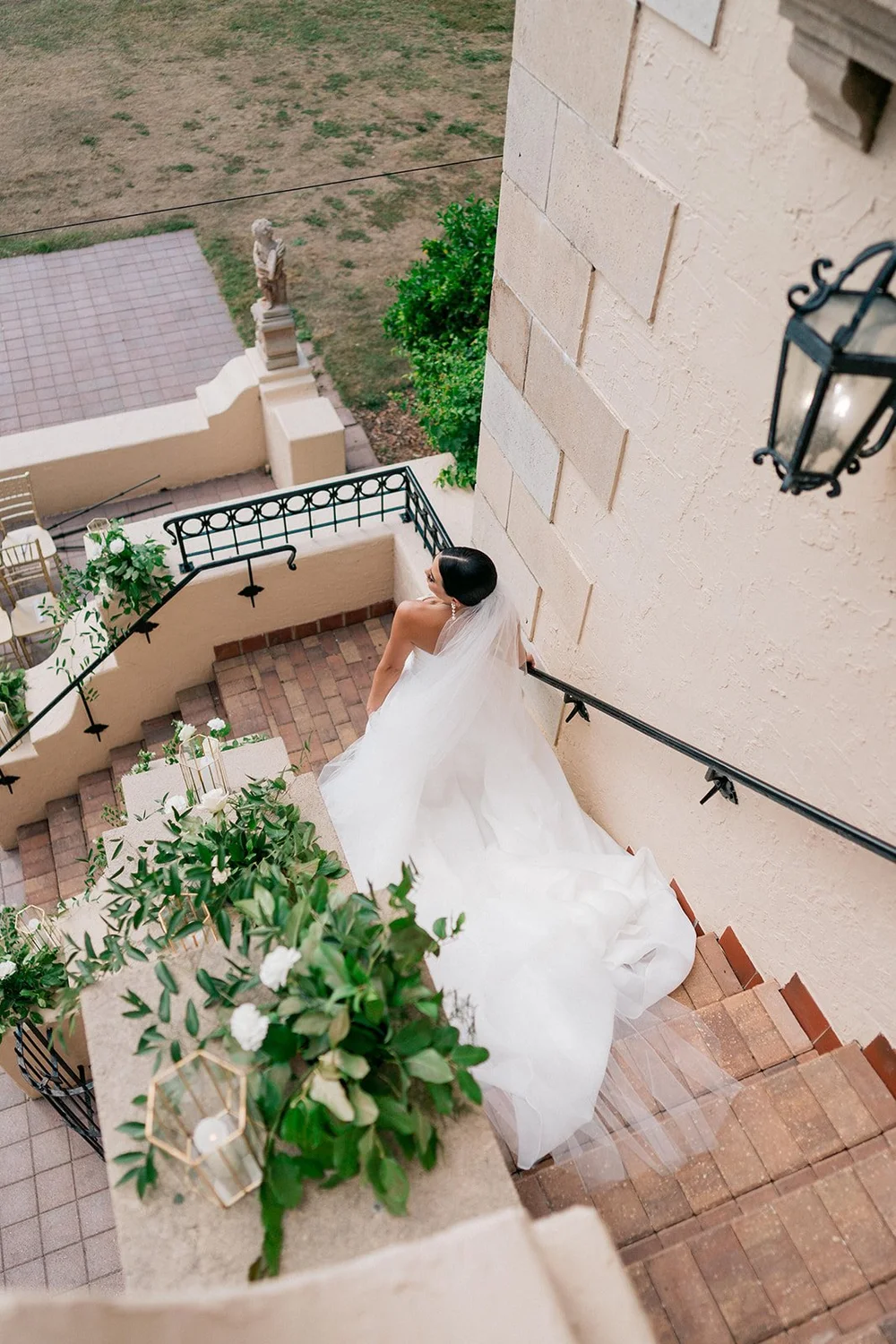 The bride in her wedding dress on an outdoor brick staircase beside the cream stucco wall of the Powel Crosley Estate