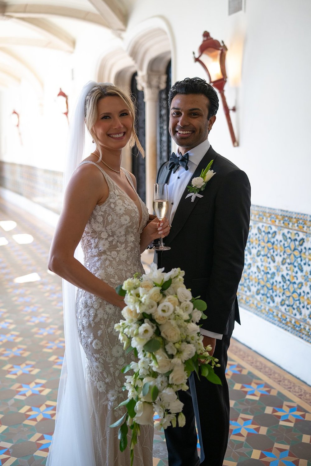 Ellen holding a white bouquet beside Jacob in a hallway with blue tile along the wall