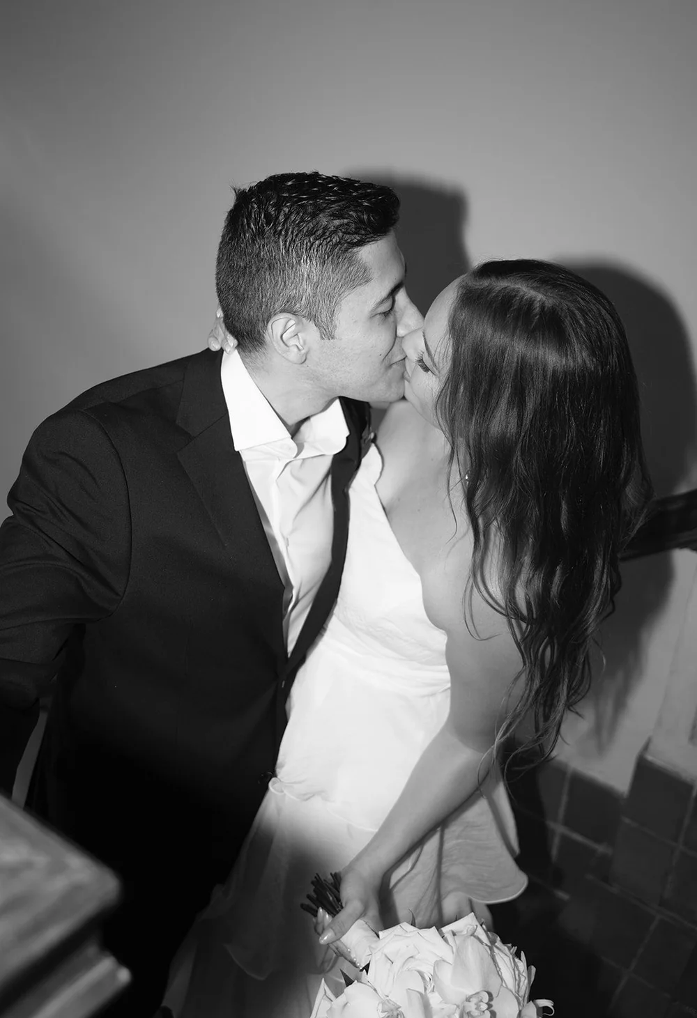 Black and white photo of David kissing Chris on a staircase landing, her hair swept across her face
