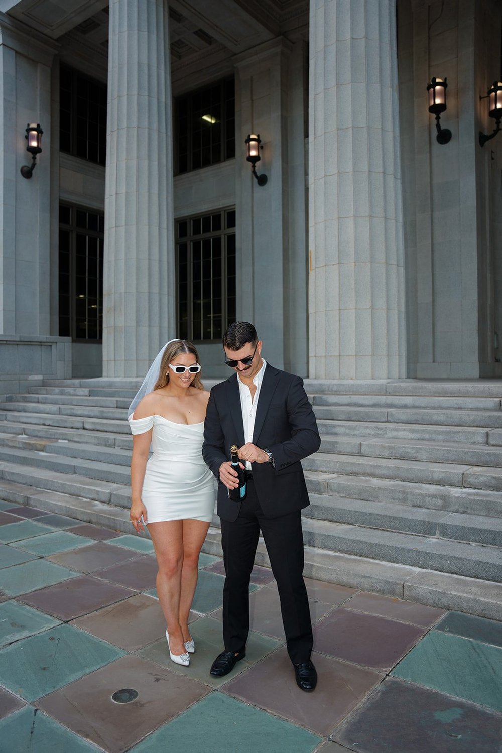 Rachel and Austin in sunglasses standing on the courthouse steps before the champagne