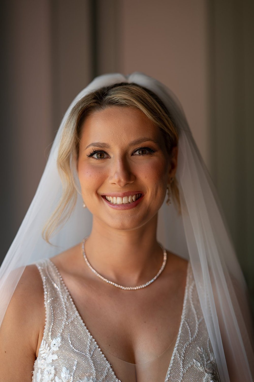 Ellen smiling in her veil and pearl necklace beside a window