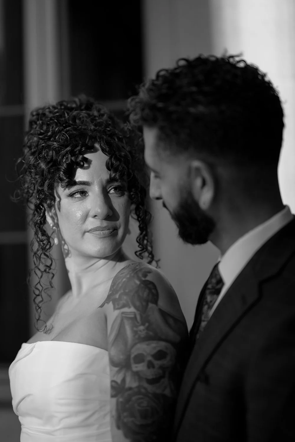 Black and white portrait of the bride looking toward the camera with the groom beside her