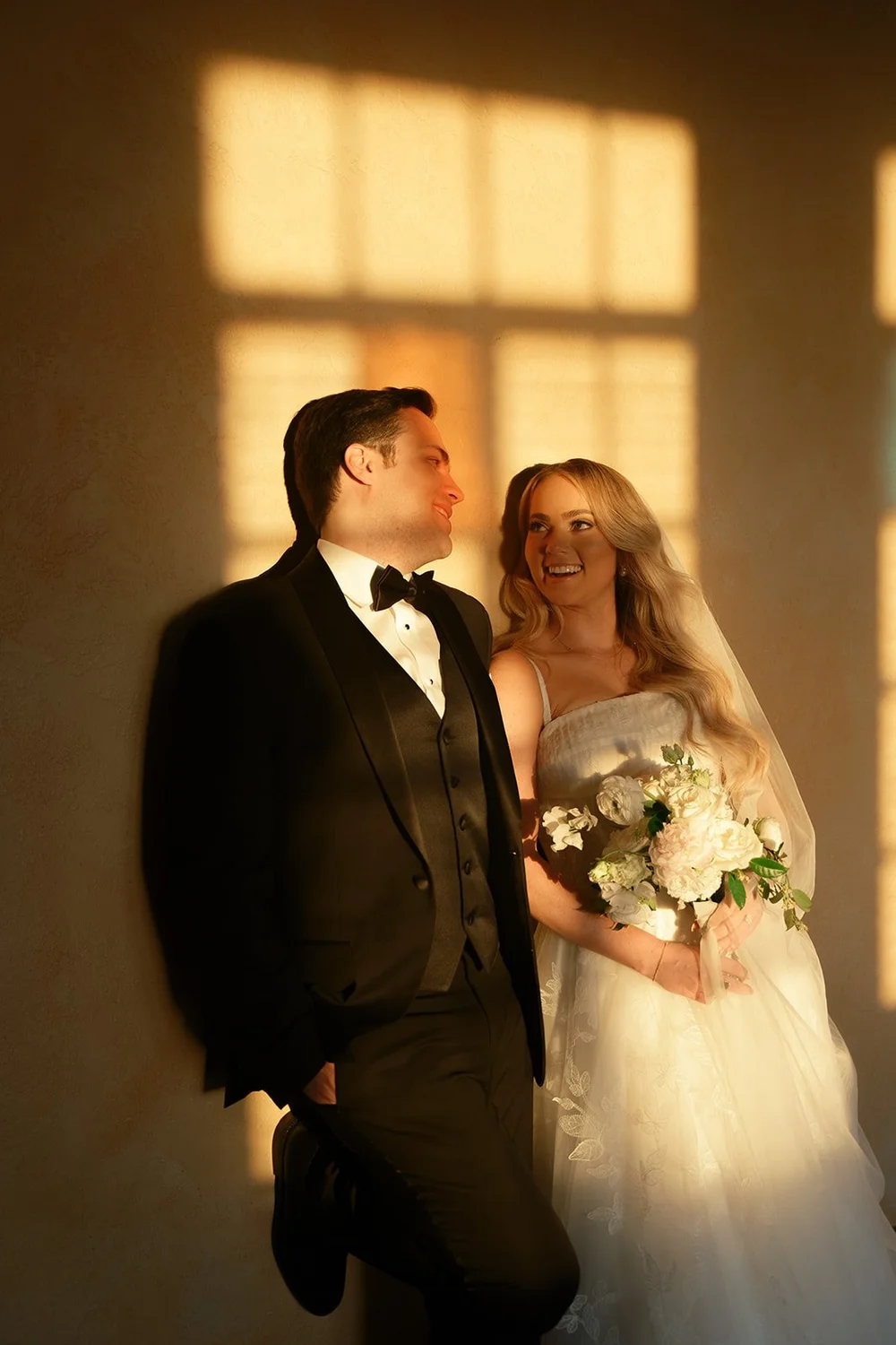 Jane and Berkeley standing together in warm golden light beside tall windows at the Powel Crosley Estate in Sarasota