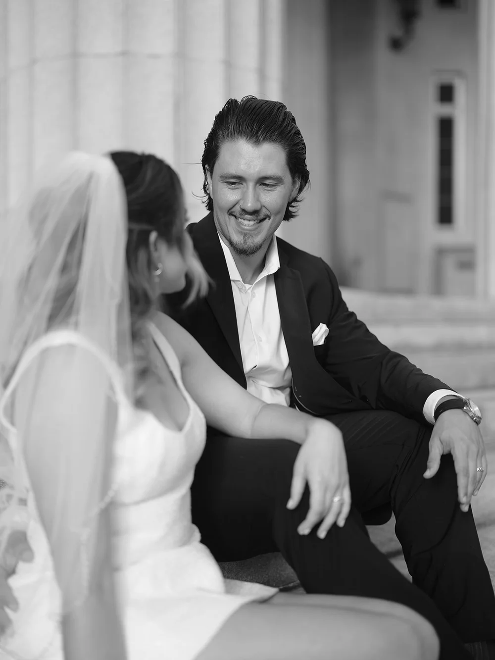 Black and white close portrait of the bride in her veil laughing while the groom smiles beside her
