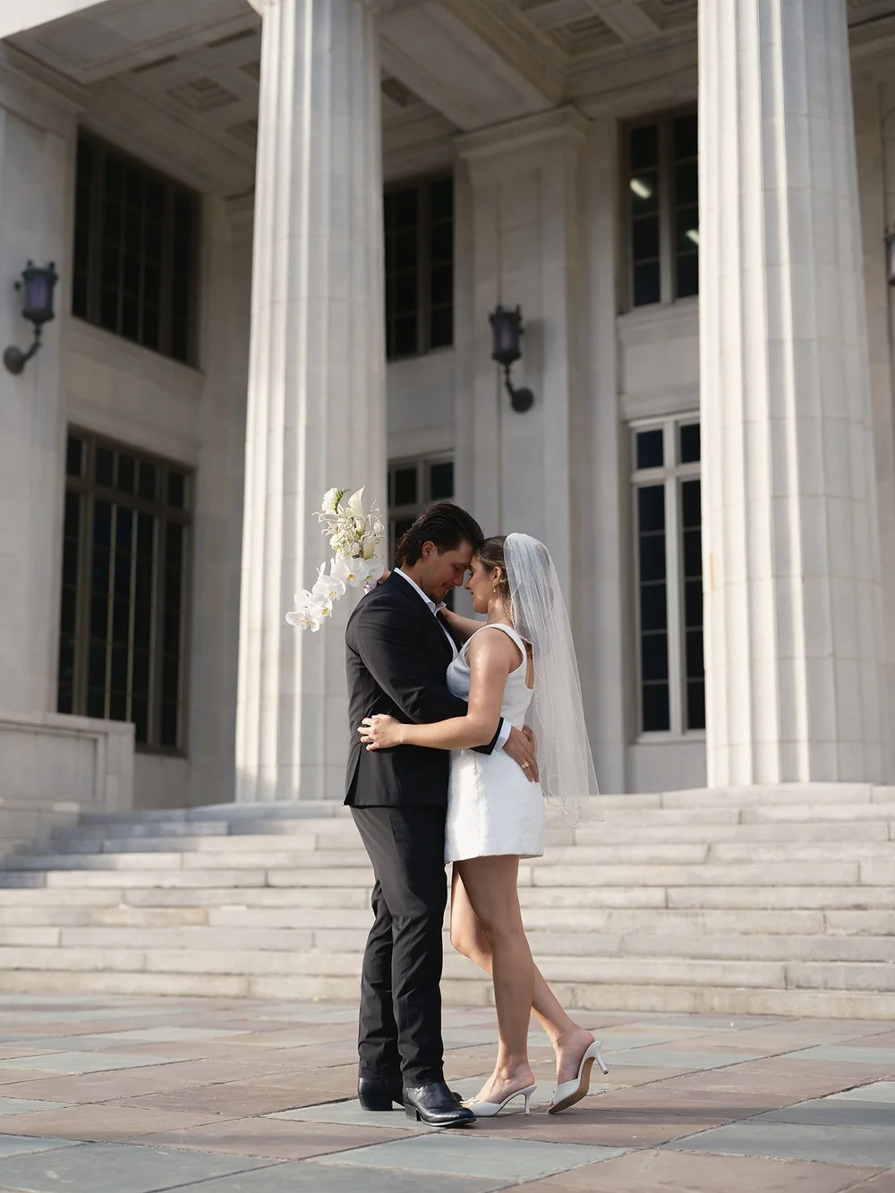 Bride and groom in an embrace at the foot of the courthouse steps with the columns behind them
