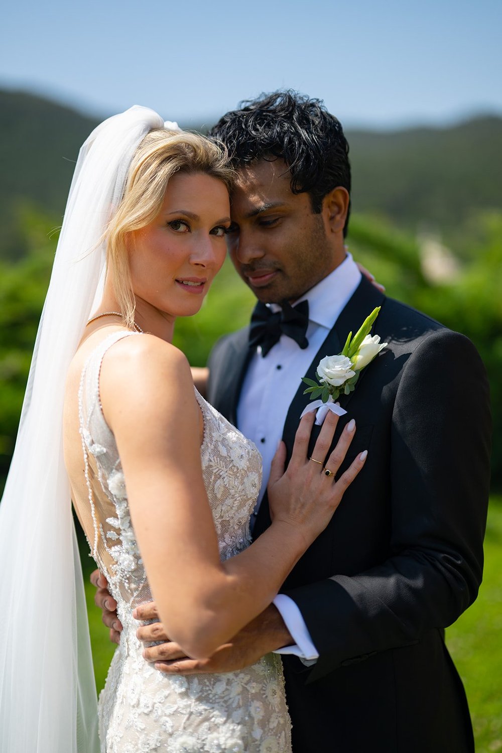 Ellen and Jacob embracing on the lawn with green hills behind them