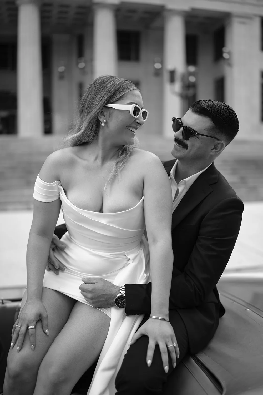 Rachel and Austin in sunglasses sitting on the Mustang, a close black and white portrait