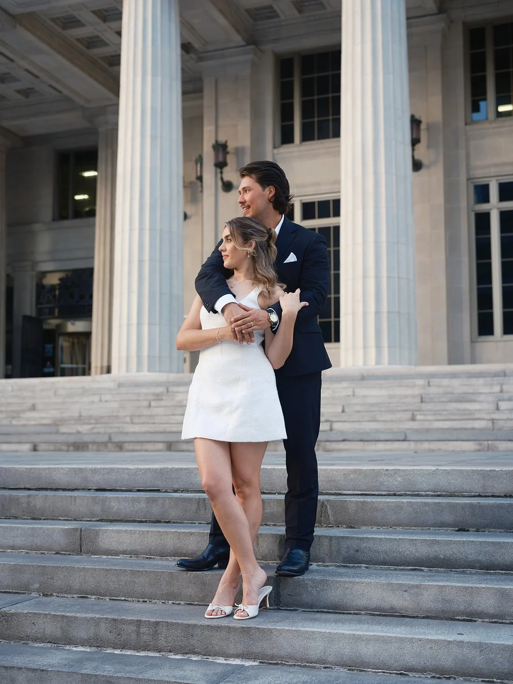 Groom embracing the bride from behind on the steps in front of the courthouse columns