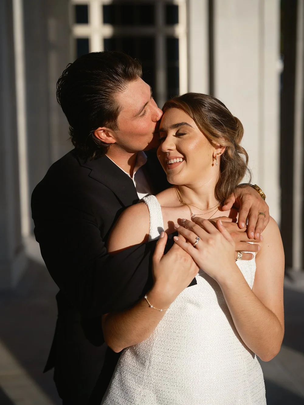Groom kissing the bride's cheek as she laughs, her hands over his arms