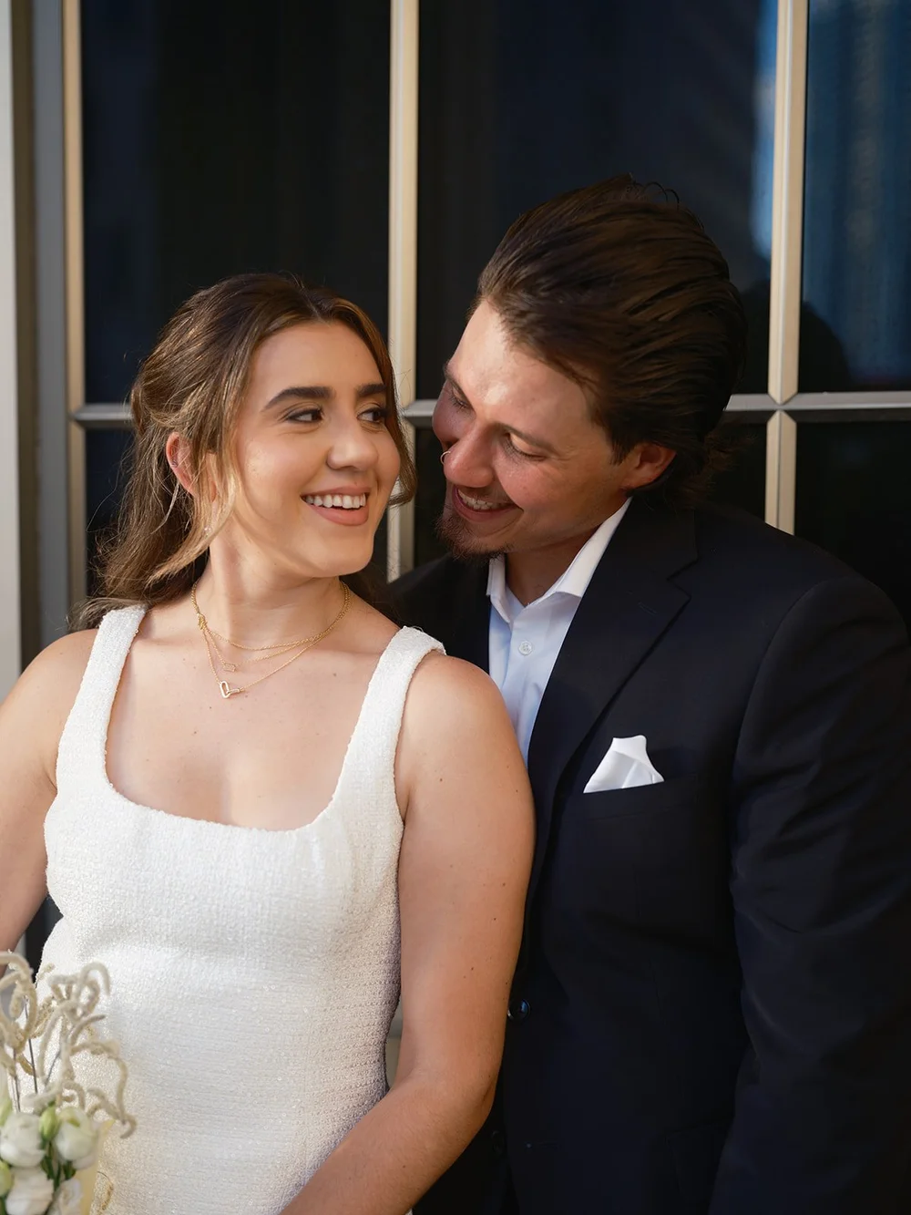 Close portrait of the bride smiling with her bouquet while the groom leans against her