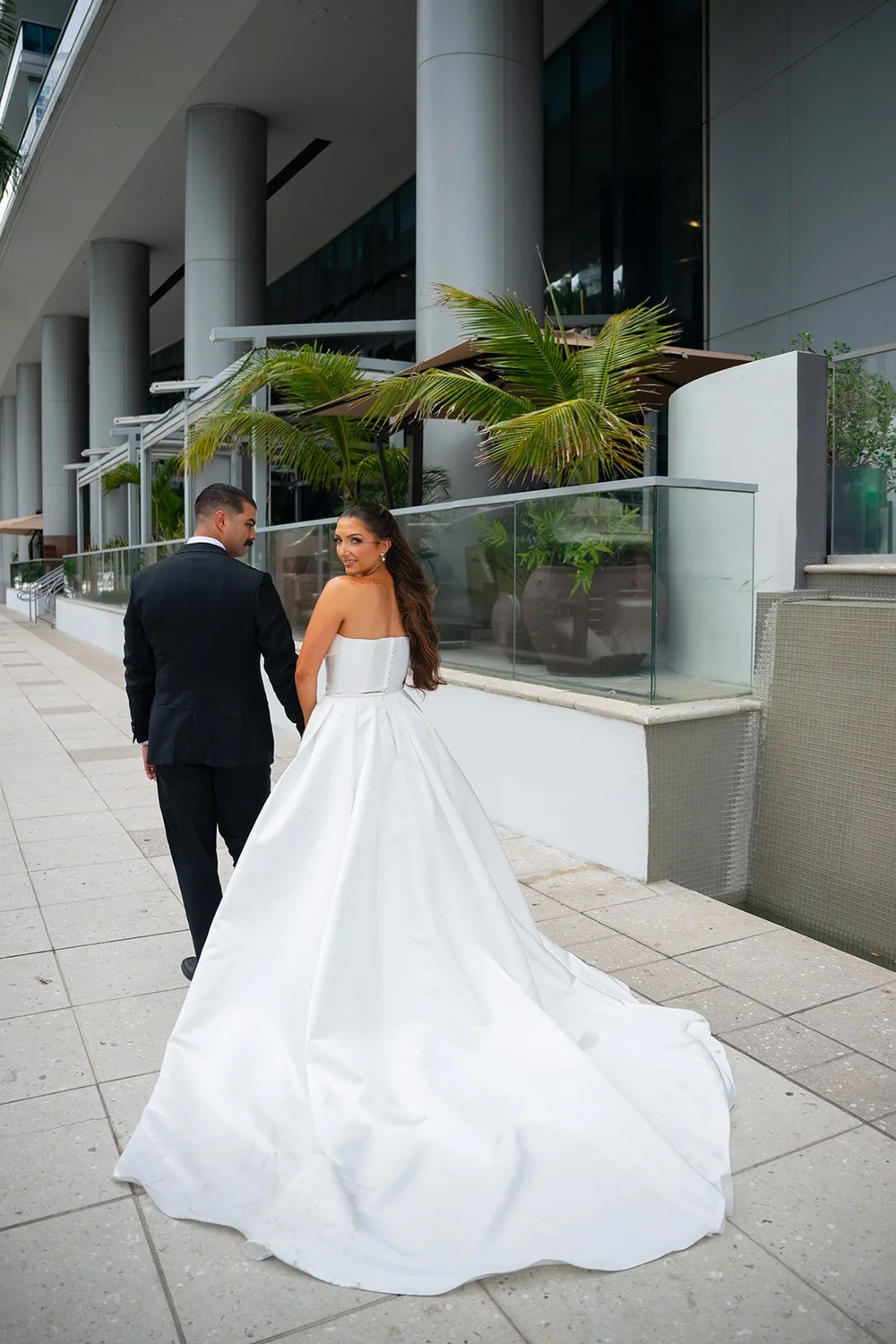 Rachel in her strapless gown with a long train walking along a terrace while Austin walks ahead