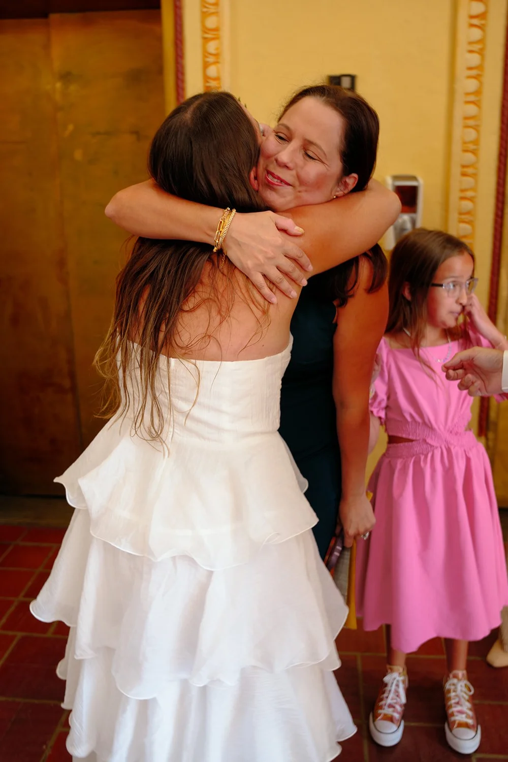 Chris hugging a family member in the hallway while a girl in a pink dress stands beside them