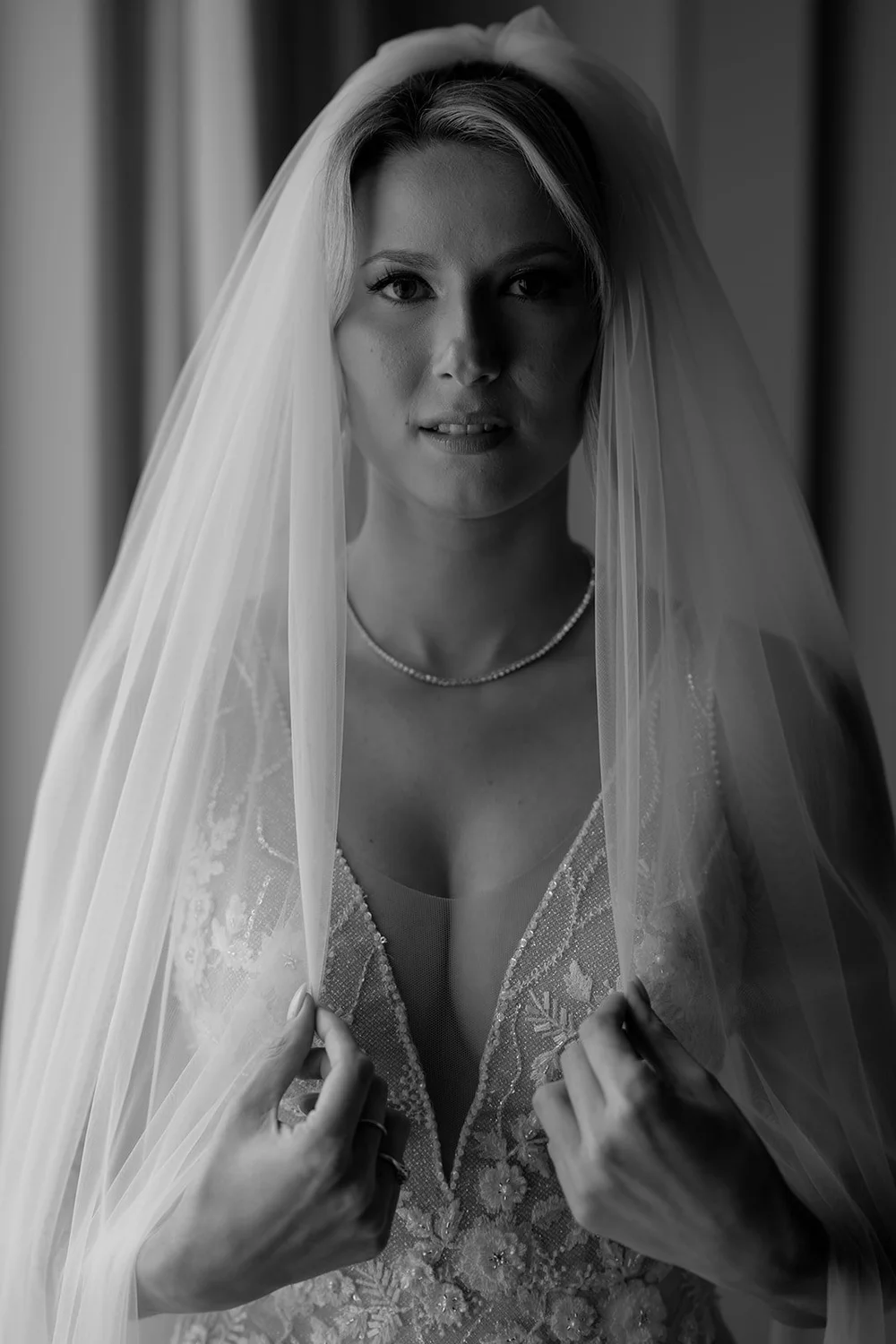 Black and white portrait of Ellen holding her veil open over her beaded wedding dress