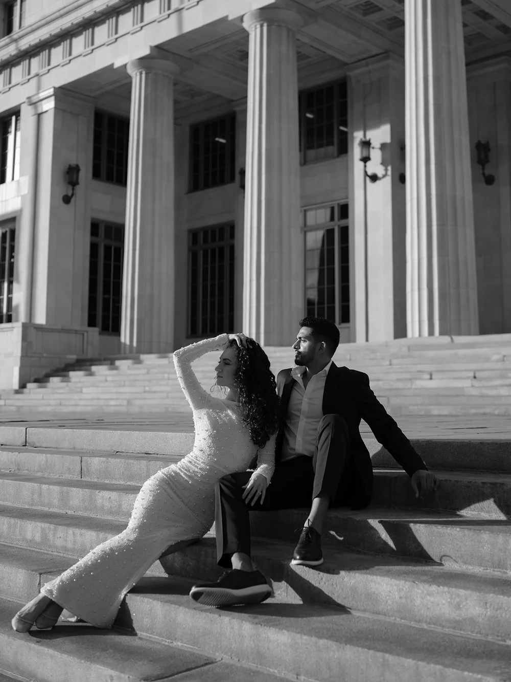 Black and white wide photo of the bride stretched out on the courthouse steps while the groom sits beside her under the columns
