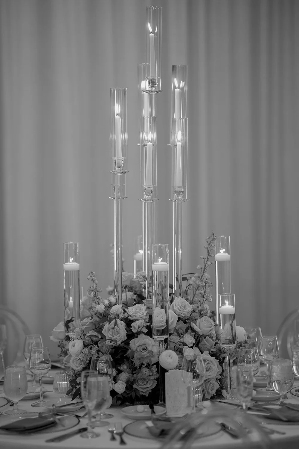 Tall glass candle holders and flowers on a reception table, in black and white