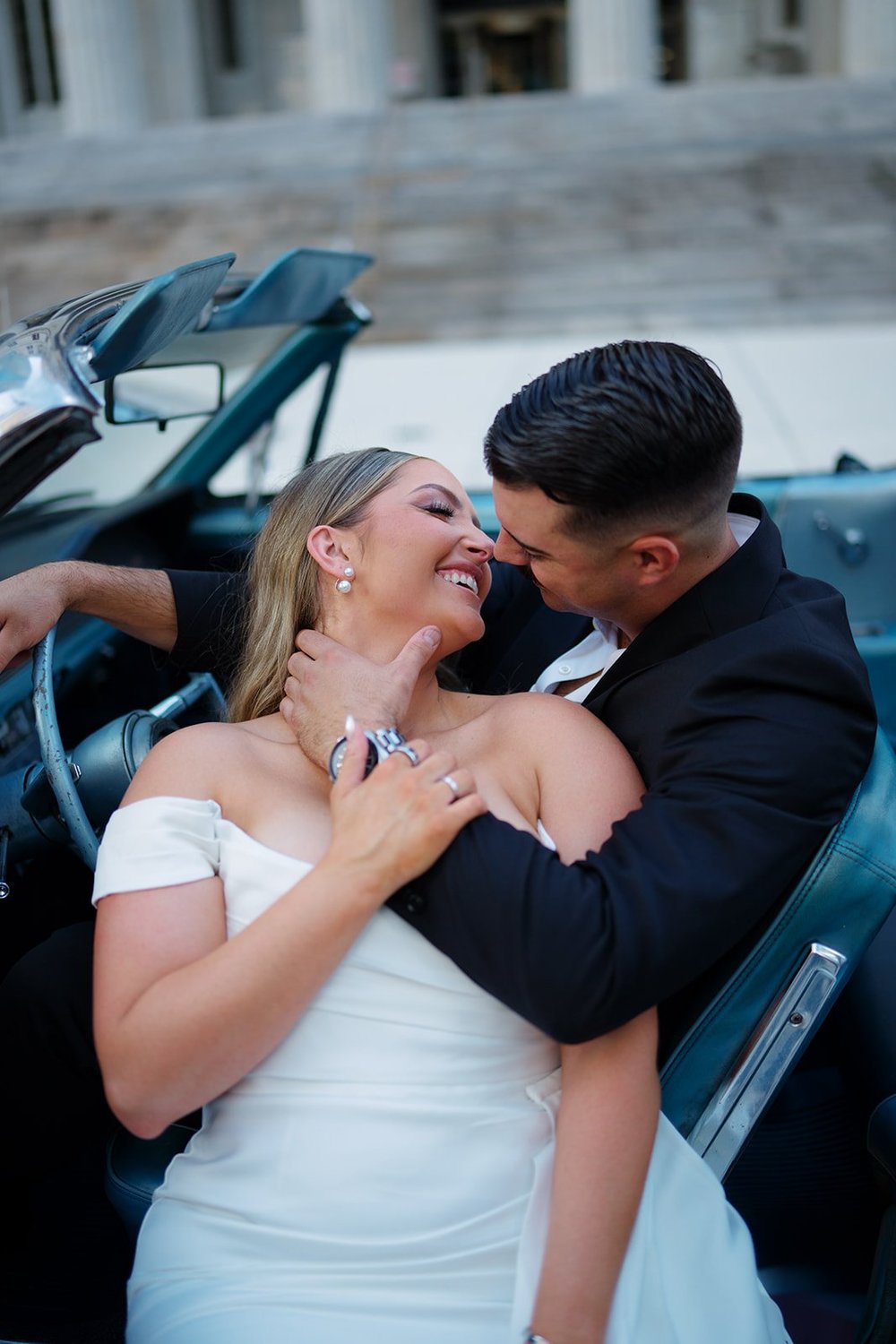 Rachel and Austin laughing in an embrace inside the blue Mustang convertible