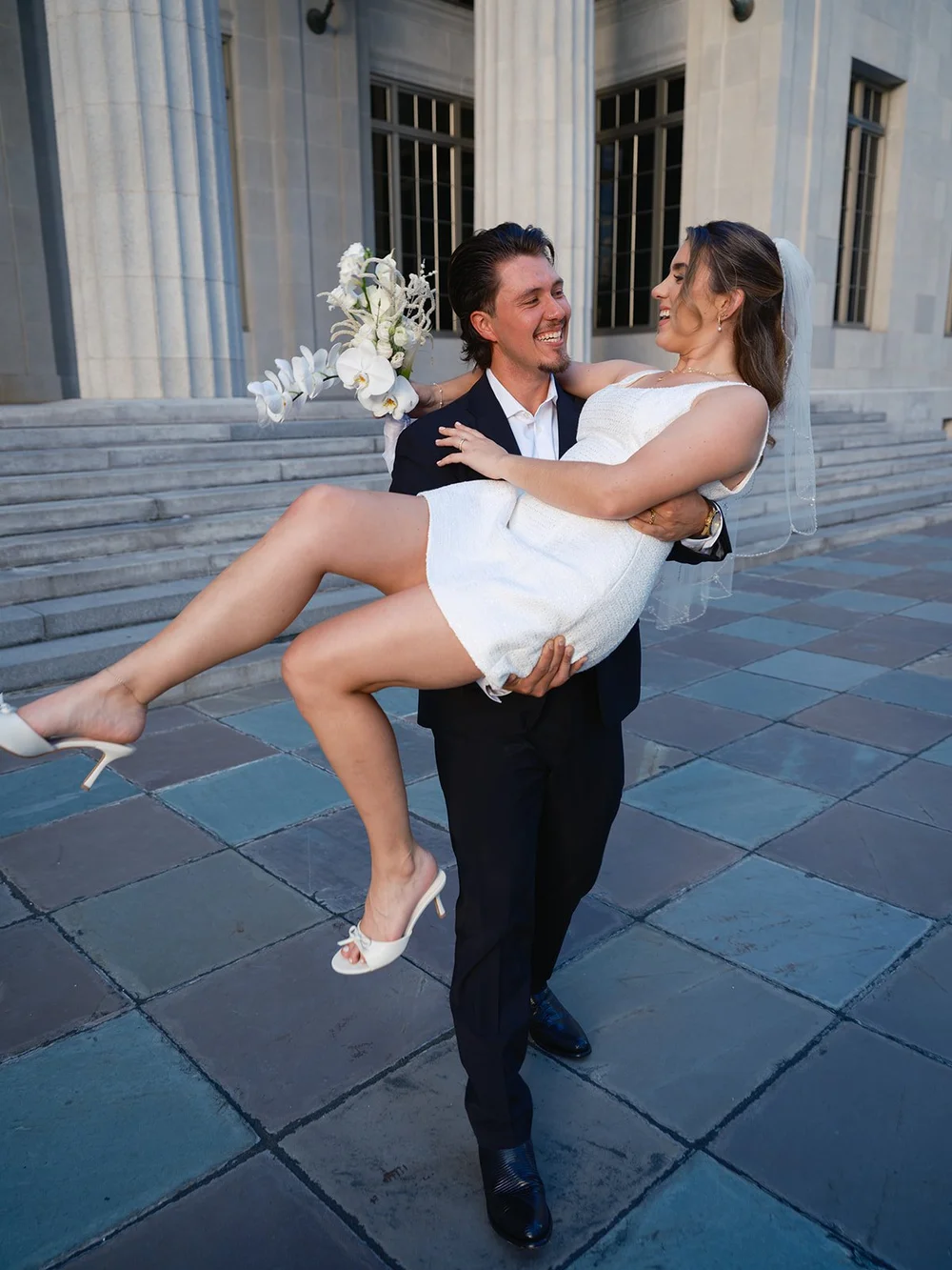 Groom lifting the bride in his arms on the stone plaza in front of the courthouse