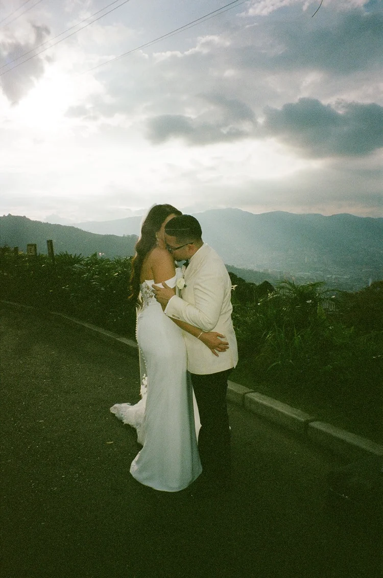 Film photo of Krystine and Douglas embracing at sunset with the Medellín mountains and clouds behind them