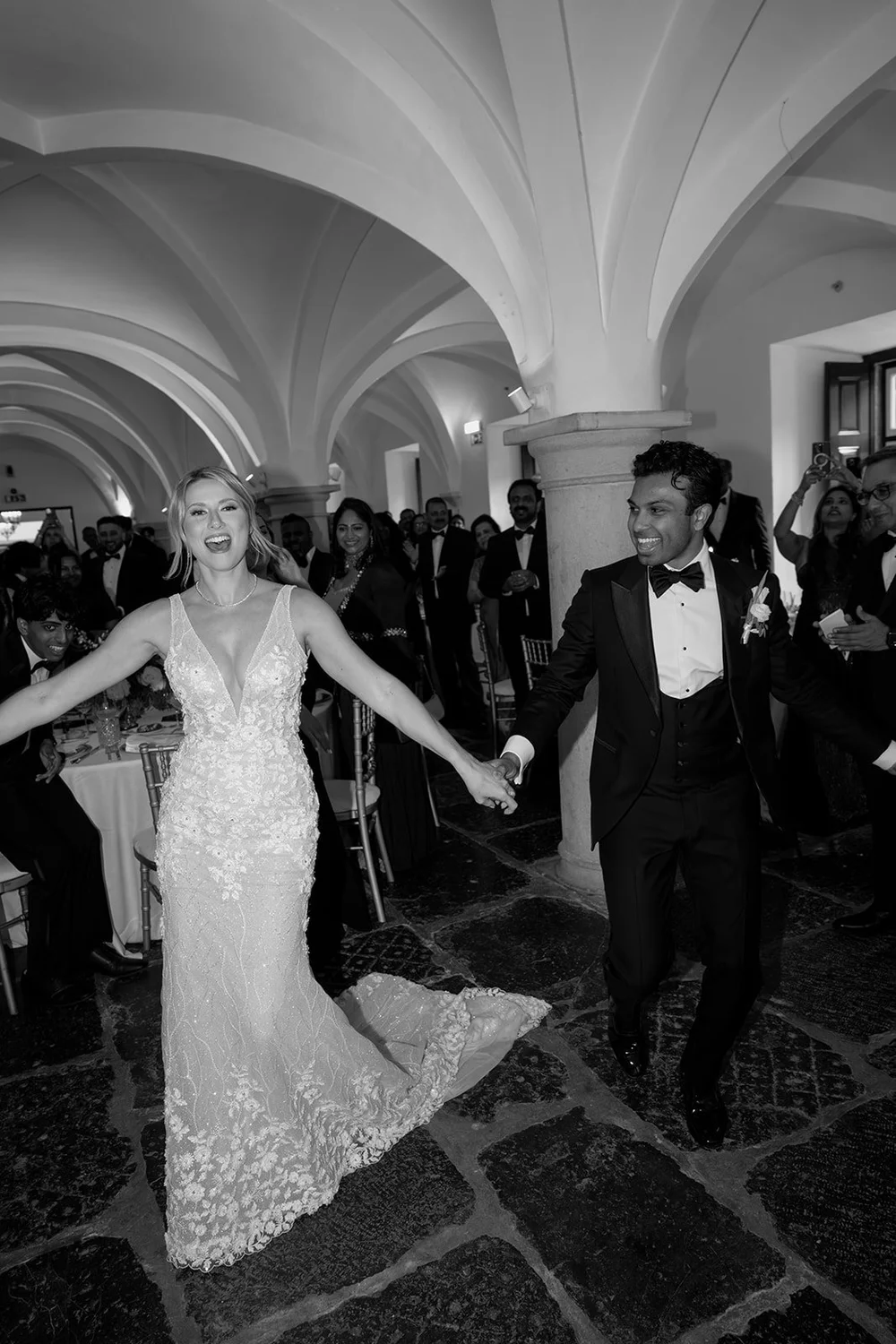 Black and white photo of Ellen leading Jacob by the hand across the reception floor
