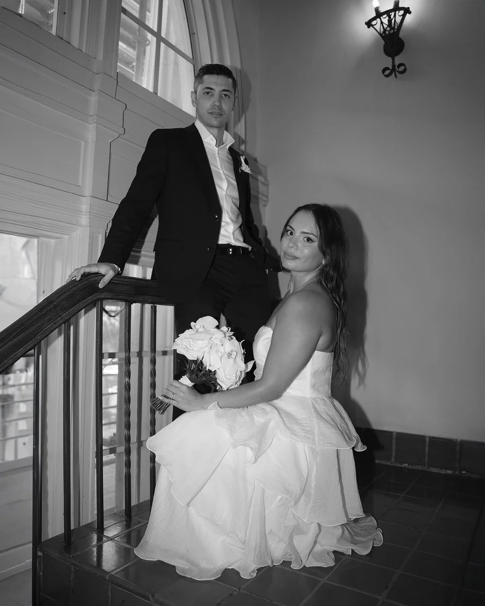Black and white photo of Chris sitting on the stairs with David standing above her at the railing