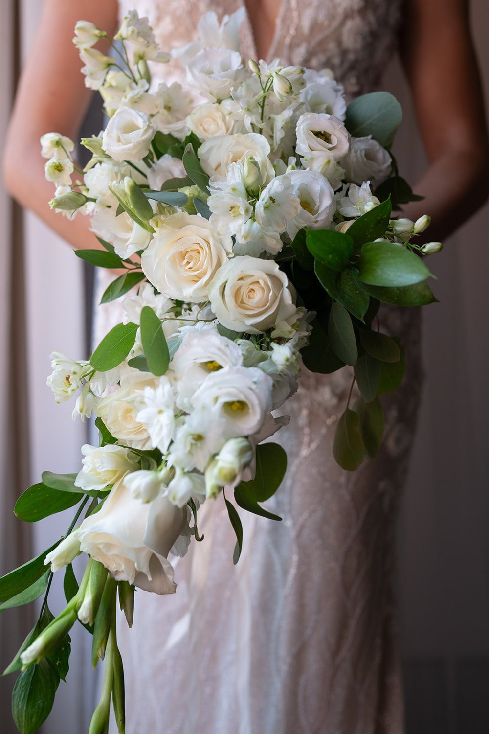 Ellen holding a bouquet of white roses in front of her beaded wedding dress