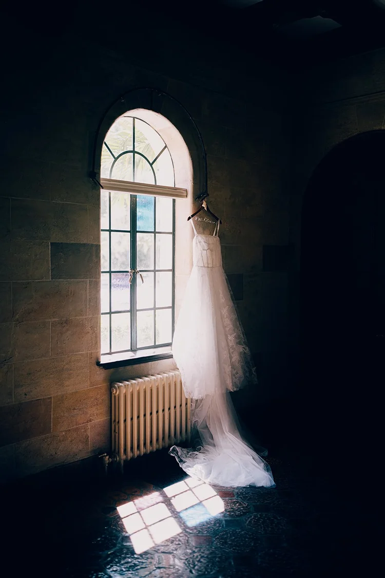 Film photo of a wedding dress hanging by an arched window with sunlight on the floor