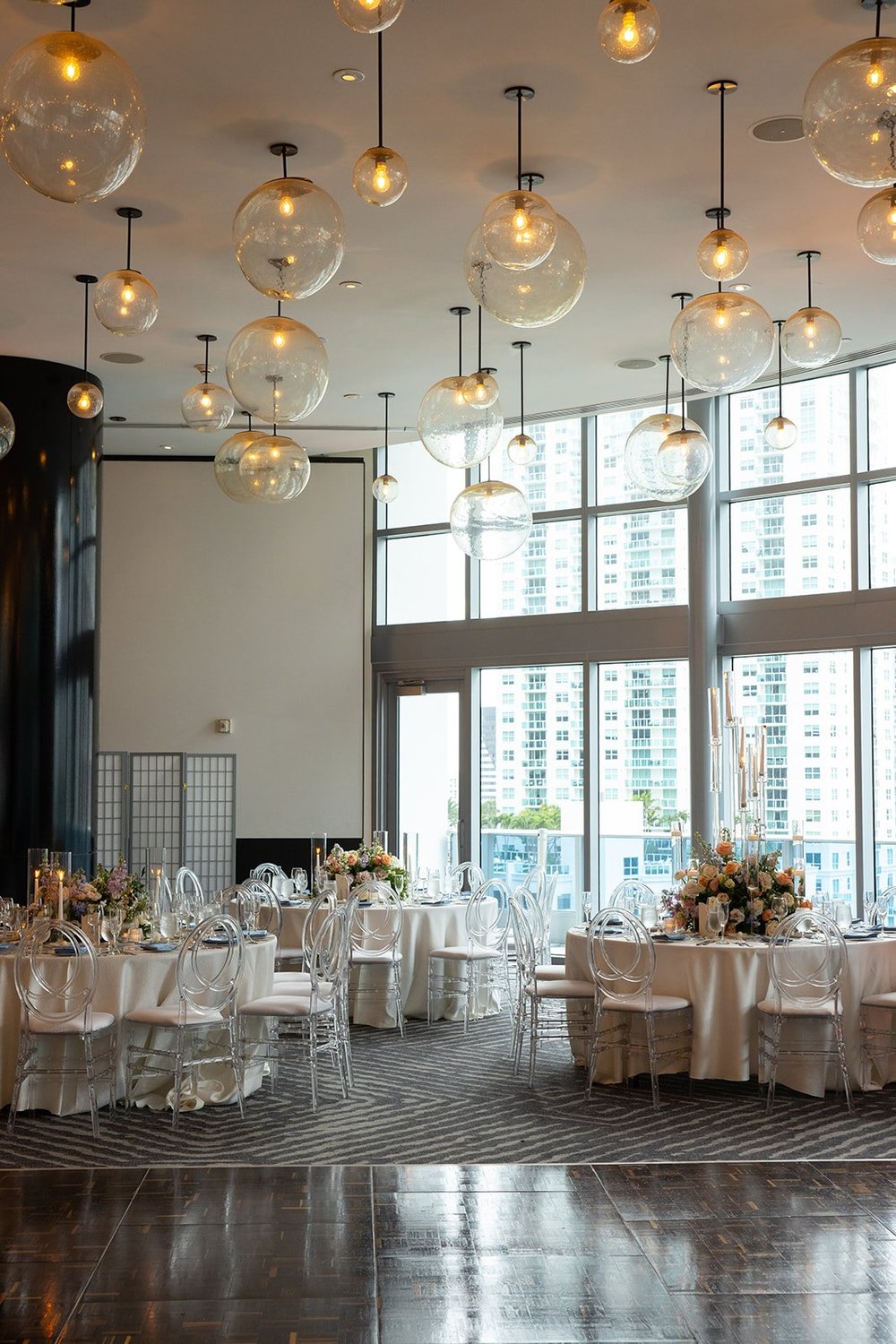 Reception room with round tables set under a ceiling of hanging globe lights and large windows