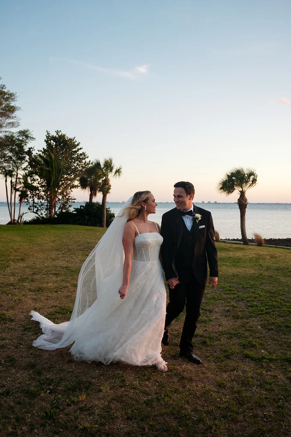 Jane and Berkeley standing together on the lawn by the water as the sky glows behind them