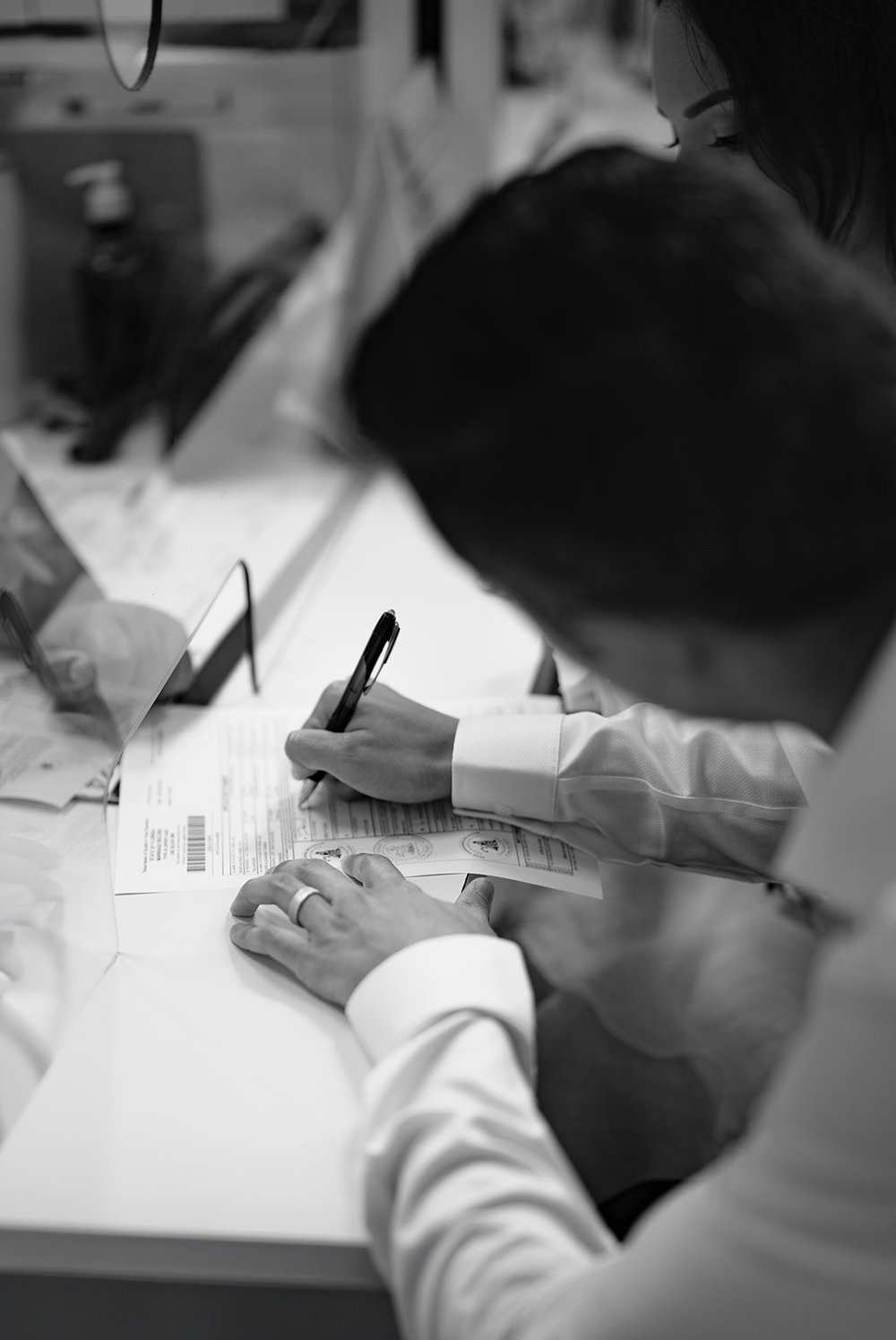 Black and white detail of hands signing paperwork at a desk