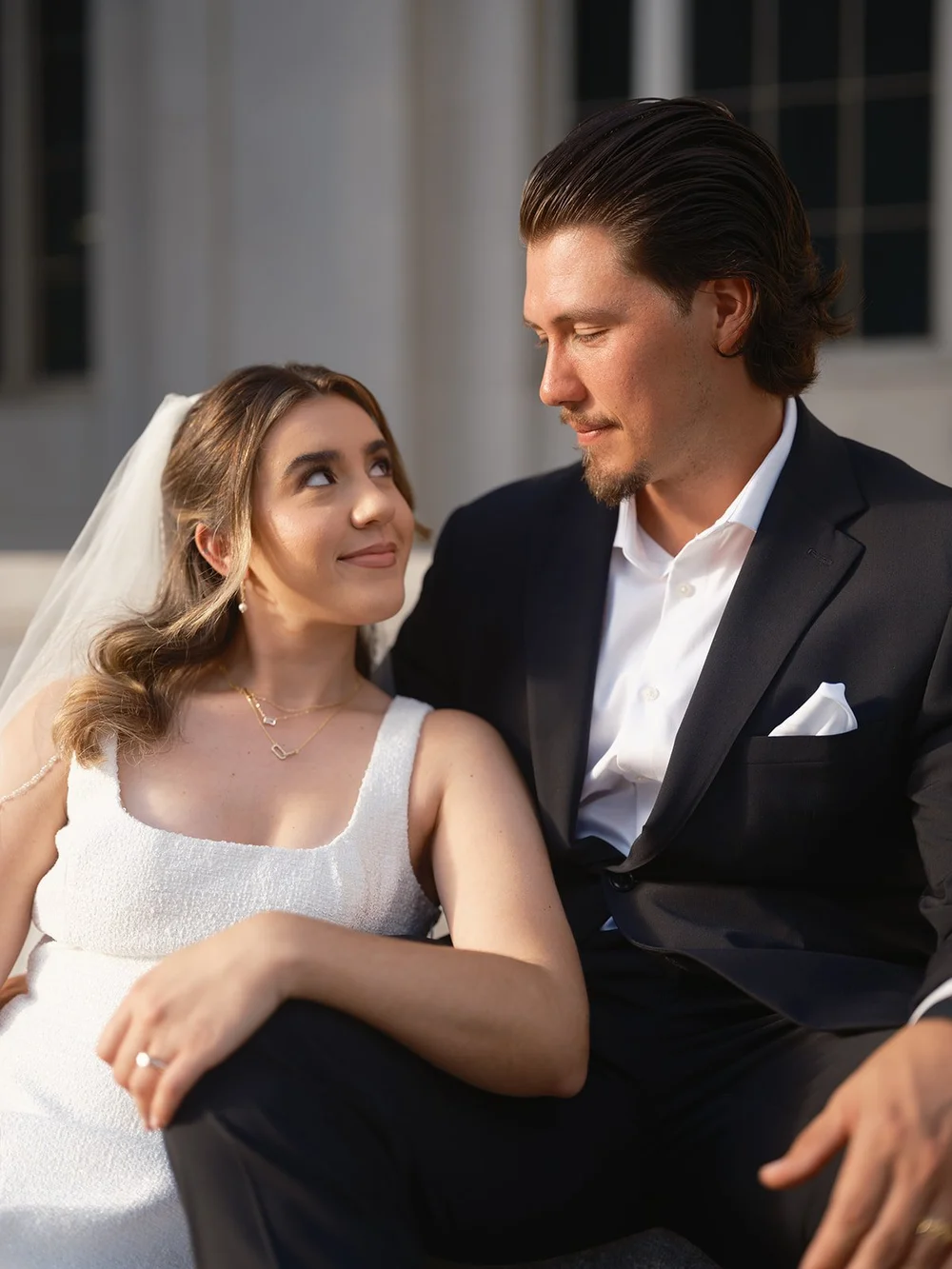 Bride in a white dress glancing up with a soft smile as the groom leans toward her